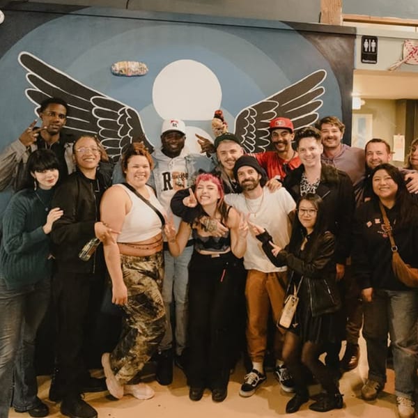 A large group of diverse people smiling and posing in front of a mural with angel wings.