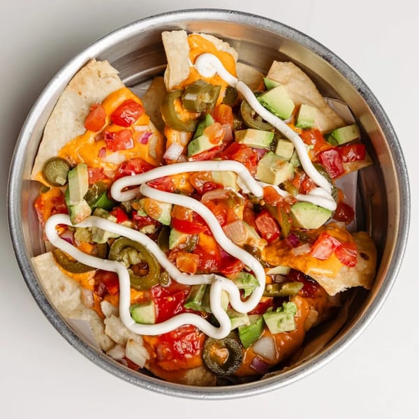 Tipsea's nachos in a metal bowl, topped with cheese, salsa, avocado, jalapeños, and sour cream.