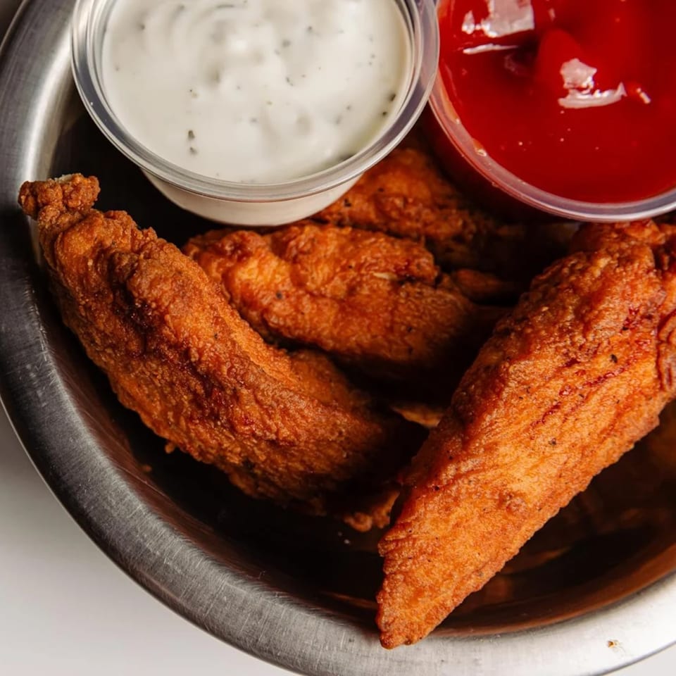 Crispy fried chicken tenders with ranch and ketchup dipping sauces in a metal bowl at Tipsea.