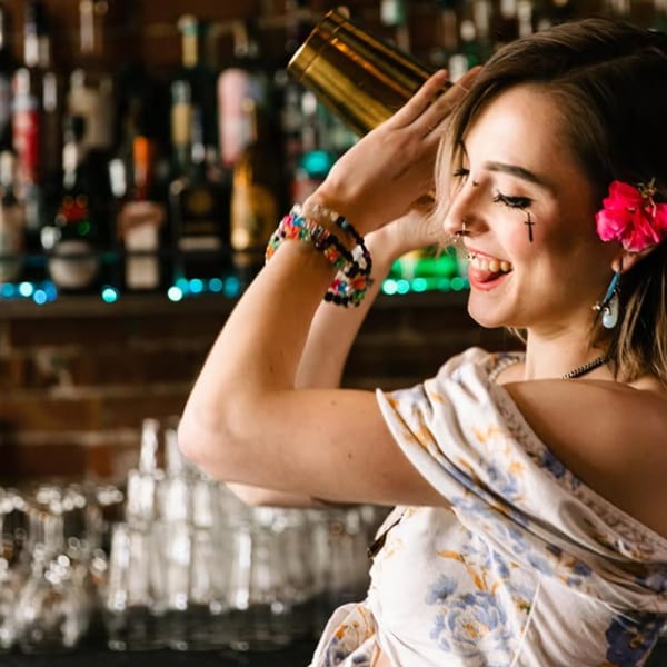 A smiling bartender with a flower in her hair shakes a cocktail shaker at Tipsea bar.